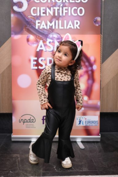 Niña delante del cartel del quinto congreso anual ASMD España 2025